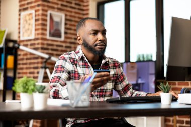 Siyah girişimci, uzaktan çalışan, banka kartı tutan ve bankacılık bilgilerine masaüstü monitöründen erişen biri. Afrikalı Amerikalı adam dijital ödeme ve otel rezervasyonu yapıyor..