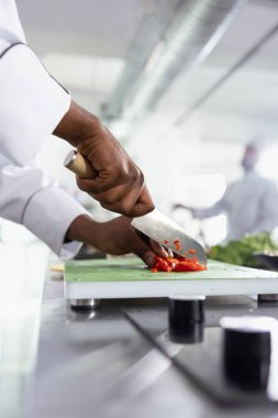 Afro-amerikan şef kesme tahtasındaki bıçakla çiğ sebzeleri doğruyor, mutfak tezgahında taze ürünleri kesiyor. Gurme yemek ve aşçılık sanatı için kullanılan bitkiler ve malzemeler.