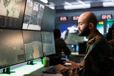 Telsiz ve uydu teçhizatı kullanarak savaş desteği sağlayan ordu telekomünikasyon sistemleri operatörü. İletişim ağlarını yöneten askeri sevk memuru, ekranlara bakıyor.