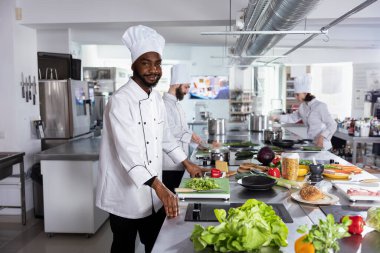 Kara şef paslanmaz çelik mutfak tezgahında durur ve bir gurme yemek yemeği için malzemeler hazırlar, ustalıkla lezzetli yemekler pişirir hassasiyetle ve yaratıcılıkla. Lezzetli gastronomi.