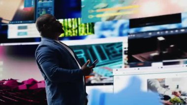 Çevrimiçi bağlantının görsel temsilini sunan genç siyahi kişi web platformları ve uygulamalarına dalmış durumda. Mobil teknoloji, dijital ortamda sosyal ağ simgeleriyle çevrili. Kamera B.