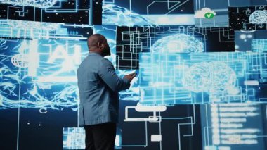 Gösterge panelinde dijital yapay zeka arayüzünü inceleyen siyah erkek bilişim mühendisi, nöral ağları, bilimi ve algoritmik düşünceyi sembolize ediyor. Yüksek teknoloji makine eğitimi için sibernetik. Kamera A.