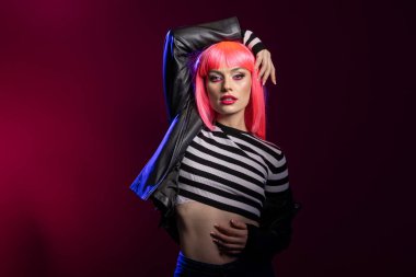 Güçlü zarif kadın, stüdyoda kendine güvenen duruşu ve cesur ifadeyi kullanarak tavır sergiliyor. Pembe saçlı, siyah deri ceketli, izole edilmiş arka planda duran vahşi bir kadın model..