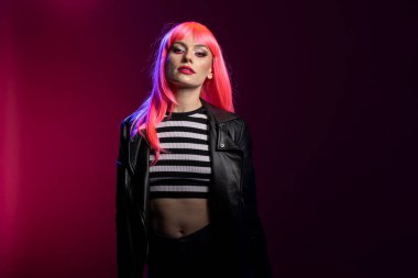 Kendine güvenen bir kadın model, göz teması ve keskin bir stil ile cesur bir tavır sergiliyor. Pembe saçlı ve çizgili popolu güzel bir kadın yaratıcı mavi ve mor stüdyo ışıklarının altında poz veriyor..