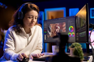 Yaratıcı medya bürosunda çalışan videograf müzik dinliyor, renk düzeltmesi yapıyor. Video düzenleyici kulaklık takıyor video düzenleyicileri düzenliyor, kliplerden montaj yapmak için yazılım kullanıyor