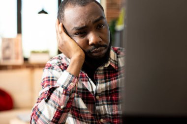 Yorgun kara girişimci, dijital cihaz ekranına bakıyor ve e-postaları ve piyasa raporlarını inceliyor. Bilgisayarlara bakarak uzaktan yapılan çalışmalardan bunalmış genç erkek yetişkinlerin yakınlaşması.