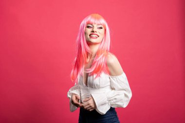 Pembe saçlı çekici beyaz kadın izole edilmiş arka planda zevkle poz veriyor. Elleri bir arada güzel bir kadın, neşeli bir ifadeyle sevimli bir model duruşu sergiliyor..