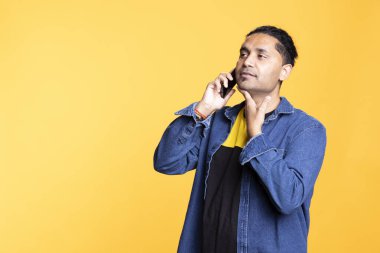 Arkadaşlarıyla konuşurken gülümseyen Hintli bir insan, telefon hattında turuncu bir arka planda sohbet ediyor. Genç bir yetişkin ve sıradan giyinmiş bir adam. Dedikodu yapıyor..