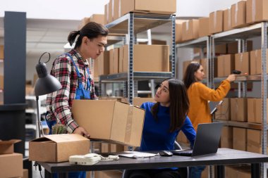 Asyalı işçi takımı kompakt envanter odasında iş lojistiği ile ilgilenir, kutuları kaydeder ve nakliye etiketleri takar. Küçük ölçekli depo personeli perakende mal teslimatını garanti ediyor.