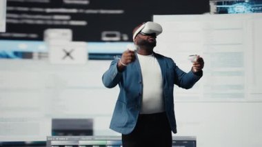 Afrika kökenli Amerikalı yazılım geliştiricisi sanal gerçeklik kulaklığını yüksek teknoloji arayüzü çalışma alanı olarak kullanıyor. Terminal pencerelerle çevrili, dijital programlama kültürünü temsil ediyor. Kamera A.
