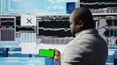 Afrika kökenli Amerikalı iş adamı KPI metriklerinin yanındaki yeşil ekranı kullanarak, şirketin yüksek kalitede bir yaşam sürmesini sağlıyor. Genç girişimci, fintech projeksiyonlarını inceliyor. Kamera A.