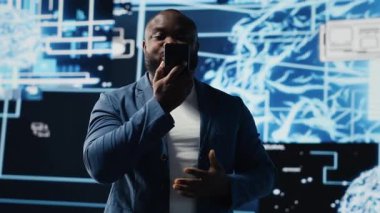 Genç siyahi iş adamı telefonla konuşuyor, yapay zeka sistemleri ve makine öğrenimi hakkında bilgi paylaşıyor. IT mühendisi sinirsel ağlar hakkında konuşuyor. Kamera B.