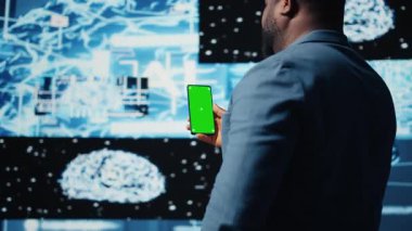 Odaklanmış siyah bilişim uzmanı, dijital yapay zeka ortamında duran yeşil ekranlı telefona bakıyor. Büyük veri otomasyonu için derin öğrenme görevleri çözmek. Sibernetik. Kamera A.