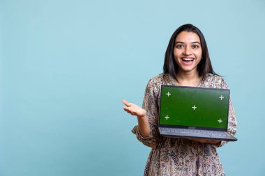 Stüdyodaki bir cihazda, stüdyonun arka planında duran yeşil ekranı sunan bir kadın etkili. Marka reklamları için fotokopi alanı kullanan hevesli genç kişi.
