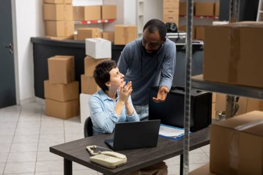 Yerel bir iş ekspres teslimatında çalışan iki farklı çalışan, küçük bir depoda bantlanmış kutular ve envanter raflarıyla çevrili. Sanayi dağıtım lojistiği.