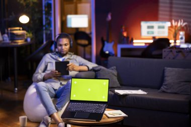 Afro-Amerikalı adam yeşil ekranın yanında müzik dinliyor, oturma odasındaki fasülye torbasında kendini rahatlamış hissediyor. Modaya uygun dairesinde oturan mutlu soğuk adam..