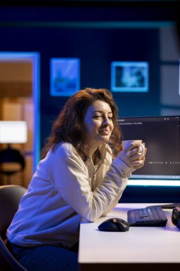 Gülümseyen bilişim teknolojileri yöneticisi kahve içerken aynı zamanda yazılımdaki savunmasızlıkları tamir ederek hackerların işletim sistemini tehlikeye atıyor. Evdeki neşeli kadın sıcak içecekten hoşlanıyor, bilgisayar kullanıyor.