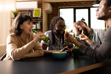 Çeşitli arkadaşlar konuşuyor, gülüyor ve tuğla duvar odasında sıradan takılmalar sırasında abur cubur ve bira paylaşıyorlar. Çok ırklı bir grup masanın etrafında oturmuş, hafta sonu kapalı yerlerde içki ve cipslerle eğleniyordu..