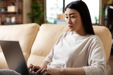 Dizüstü bilgisayarda yazan, iş analizlerini yöneten ve profesyonel e-postalara cevap veren odaklanmış bir girişimci. Rahat oturma odasında görevleri dengeleyen kendinden emin bir iş kadını..