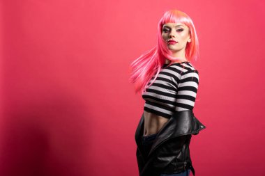 Pembe peruklu ve şık giyimli muhteşem beyaz kadın stüdyo portresinde duruyor, kendine güveni zarafetle yayıyor. Cesur makyajlı güzel bir kadın model, kameraya vahşice bakıyor..