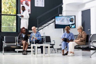 Hastane lobisinde hastaları ile görüşen siyah sağlık hizmeti sağlayıcısı, tıbbi tesisin bekleme salonunda danışmanlık ve danışmanlık yapıyor. Afrikalı Amerikalı hemşire yaşlı kadınla sohbet ediyor..