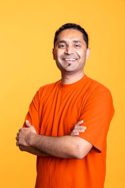 Gülümseyen ve kollarını kavuşturup stüdyonun arka planında duran neşeli Hintli adamın portresi. Neşeli, neşeli erkek kıyafetleri içinde olumlu duygular sergiliyor..