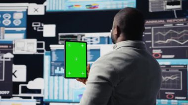 Afrika kökenli Amerikalı lider, fintech grafikleri ve KPI projeksiyonları ile çevrili, iş geliştirme için veri içgörüsüyle model ekranını inceliyor. Finansal performans ve karar verme. Kamera A.