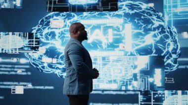 Afrikalı Amerikalı adam akıllı teknoloji yapay zeka sistemlerini sibernetik platformlar ve yapay zeka arayüzleri ile etkileşim içinde olmak için inceliyor, makine öğrenme ve tahmin analizlerinin entegrasyonunu temsil ediyor. Kamera A.