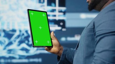 Siyahi bilişim uzmanı kroma anahtarının yanındaki algoritmik verileri inceliyor, ileri teknolojili dijital görsellerle dolu bir ortamda tablet kullanıyor. AI akıllı teknoloji ve sinirsel ağlar. Kamera B.