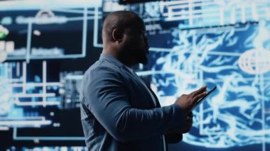 Gösterge panelinde dijital yapay zeka arayüzünü inceleyen siyah erkek bilişim mühendisi, nöral ağları, bilimi ve algoritmik düşünceyi sembolize ediyor. Yüksek teknoloji makine eğitimi için sibernetik. Kamera B.