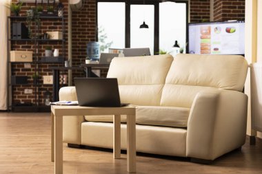 Yeni başlayan şirketteki çalışanlar için düzgün bir şekilde düzenlenmiş boş tuğla duvar çalışma alanı. Masanın yanında dizüstü bilgisayarı olan boş bir kanepe modern ofiste rahatlık ve verimliliği vurguluyor..