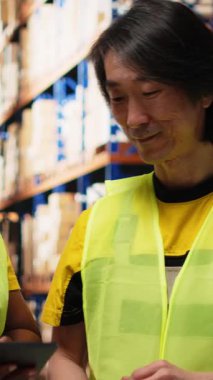 Vertical Video Diverse çalışanları dağıtım için sipariş detaylarını denetliyor, endüstriyel raflardaki dijital stok envanterlerini ve kargo paletlerini kontrol ediyor. Büyük ölçekli hızlı teslimat. Kamera B.