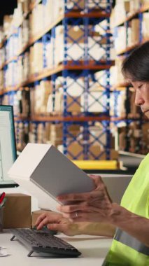 Karton kutuları doğrulayan dikey video işçisi ve paket izleme, dağıtım öncesi sipariş işleme için awb etiketleri. Yelekli bir adam e-ticaret deposunda çalışıyor.