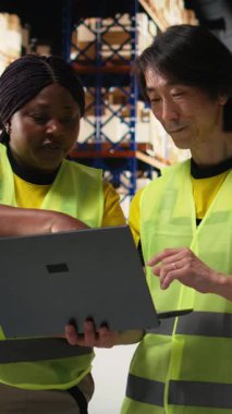 Dikey Video Afro-Amerikan ve Asyalı işçiler, dizüstü bilgisayardaki hisseleri inceleyerek ve siparişleri düzene sokarak büyük bir markanın ürünlerini işletiyorlar. Müşteriler için profesyonel hızlı teslimat. Kamera A.