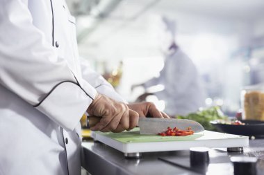 Profesyonel bir aşçı, ticari bir mutfakta taze sebzeler doğruyor. Güzel bir restoran yemeği için kaliteli malzemeler sağlıyor. Genç adam çiğ sebze ve ot doğruyor ya da doğruyor..