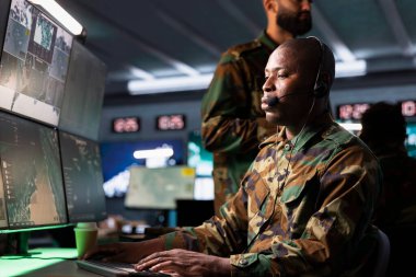 Karşı İstihbarat Teşkilatı harekat subayı ordu istihbarat analistlerinden cephe hattına bilgi aktarıyor. Afrika kökenli Amerikan telsiz iletişim operatörü mikrofonla konuşuyor.