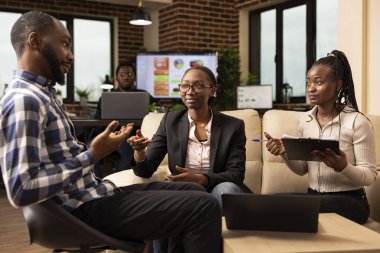 Afrika kökenli Amerikalı iş arkadaşları dizüstü bilgisayar ve panoyla ofiste oturup evrak işlerini gözden geçiriyorlar ve finansal proje raporlarını tartışıyorlar. Yoğun başlangıç takımı modern bir çalışma alanında verimli bir şekilde işbirliği yapar.