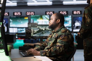 Ordu telekomünikasyon sistemleri uzmanı radyo ve uydu ekipmanları kullanıyor, savaş desteği sağlıyor. Afrika kökenli Amerikan askeri harekat subayı iletişim ağlarını yönetiyor, ekranlara bakıyor.