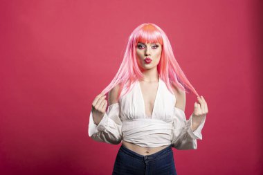 Pembe peruklu ve omuzsuz, kendine güveni tam bir kadın saçlarını tutarken somurtuyor. İzole edilmiş arka fona karşı duran muhteşem bir model. Garip bir özgüven yayıyor..