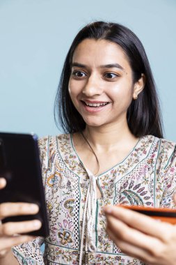 Cep telefonuna bankacılık bilgilerini ekleyen iyimser biri ödemeyi ve para transferini bir web sitesinden onaylıyor. Genç Hintli yetişkin internetten satın alıyor. Stüdyo arka planında kart kullanıyor..