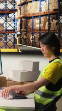 Dikey Videolu Asyalı depo çalışanı siparişleri işliyor ve teslimat işlemi için kutulara takılacak takip numaralarını uyduruyor, paket izleme yazılımında sevkiyat detaylarını kaydediyor. Tamamlama Merkezi
