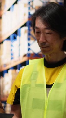 Dikey Afrikalı Amerikalı ve Asyalı ekip, sevkiyatları dijital envanter ve kargo paletleriyle birlikte depo raflarına hazırlayın. Ekspres teslimat için büyük ölçekli bir dağıtım merkezinde çalışıyor.