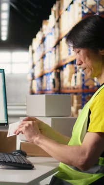 Dikey Video Dağıtım Merkezi personeli paketlere hatalı etiketler basıyor ve uyguluyor, bir depoda yelek giyiyor. Sipariş yerine getirmek için barkod havayolu faturası ve nakliye etiketleri kullanılıyor.