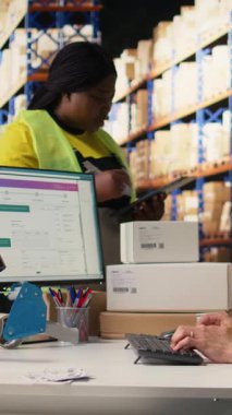 Depo arz ve talep işlemlerini tamamlayan dikey video ekibi bilgisayar monitöründen sevkiyat detaylarını kontrol ediyor. E-ticaret deposu. Kamera A.