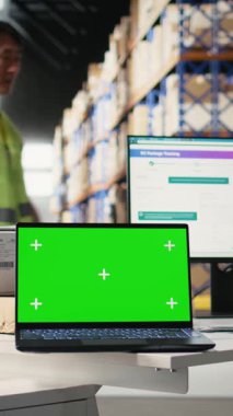 Yeşil ekran monitörünün yanındaki depo çalışanlarından oluşan dikey video ekibi. Endüstriyel depoda nakliye etiketleri, barkod tarayıcı verileri veya e-ticaret envanter izleme sistemleri yönetiliyor