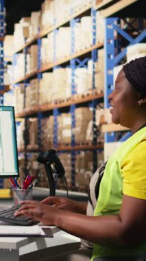 Bir dağıtım merkezinde ambalaj işlemleri sonrasında barkod sevkiyat etiketlerini kaydetmek için tarayıcı kullanan dikey Video Black çalışanı, sonraki sipariş takibi için awb etiketlerini tarıyor. Depo odası. Kamera.