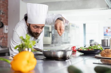 Restoran mutfağındaki baş aşçı, taze yeşillik ve baharat kullanarak ocakta yemek pişirirken tat katmak için kaplara son bir şifalı ot dokunuşu daha ekliyor. Lezzetli aşçılık sanatı.