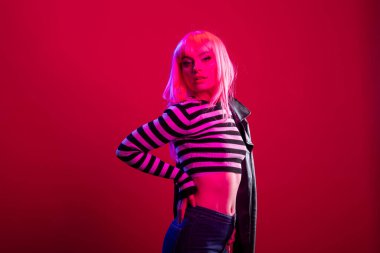 Kendine güvenen bir kadın model, canlı pembe stüdyo ışıkları altında el üstünde poz verir. Çizgili bluz ve koyu deri ceket giyen muhteşem bir kadın isyankar moda konseptini geliştiriyor..