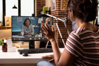 Uzaktan çalışan siyahi bir kadın, masaüstü bilgisayarındaki grup video konferansına katılıyor. Bilgisayar kullanarak iş görüşmesi sırasında iş arkadaşlarıyla konuşan profesyonel bir uzaktan kumanda yöneticisi.