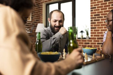 Gülümseyen beyaz adam satranç maçını kazandıktan sonra yumruğunu kaldırır. Beyaz erkek satranç tahtasına sevinçle bakıyor. Dost canlısı masa oyunu sırasındaki zaferinden memnun..